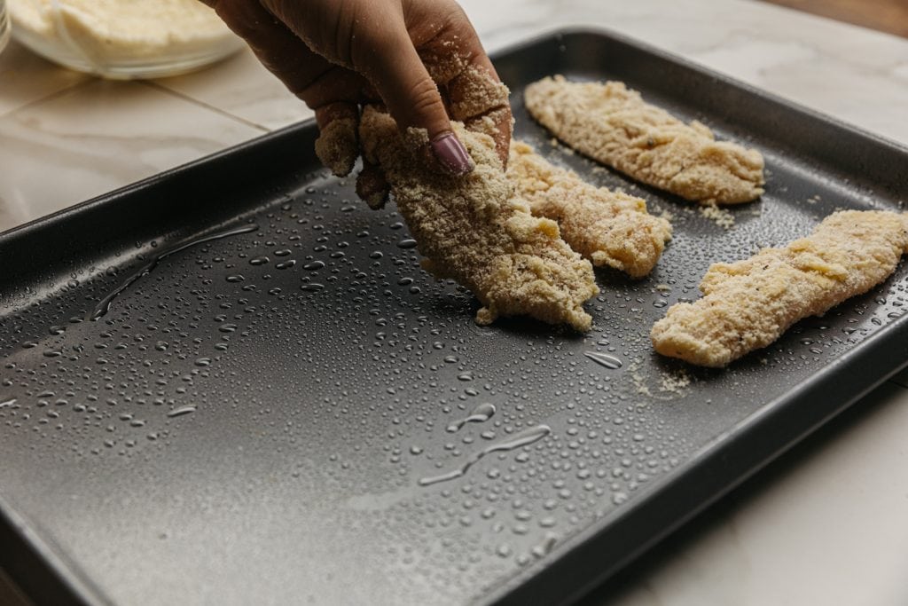 keto chicken tenders being placed on a baking sheet