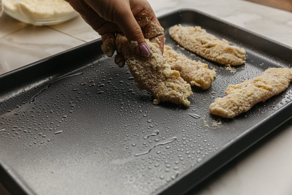 keto chicken tenders keto chicken tenders being placed on a baking sheet