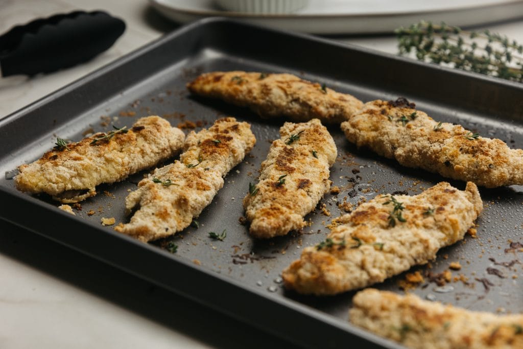 baked keto chicken tenders coming out of the oven on a baking sheet