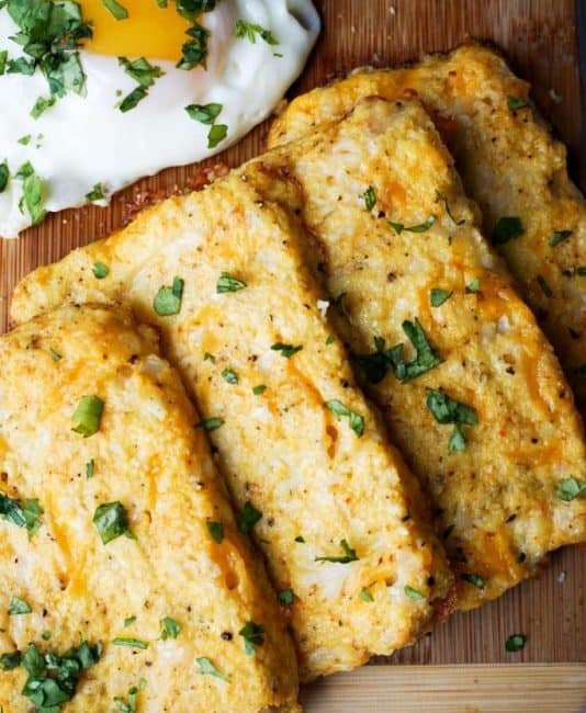Cauliflower Hash Browns four cauliflower hash browns on a cutting board with an egg