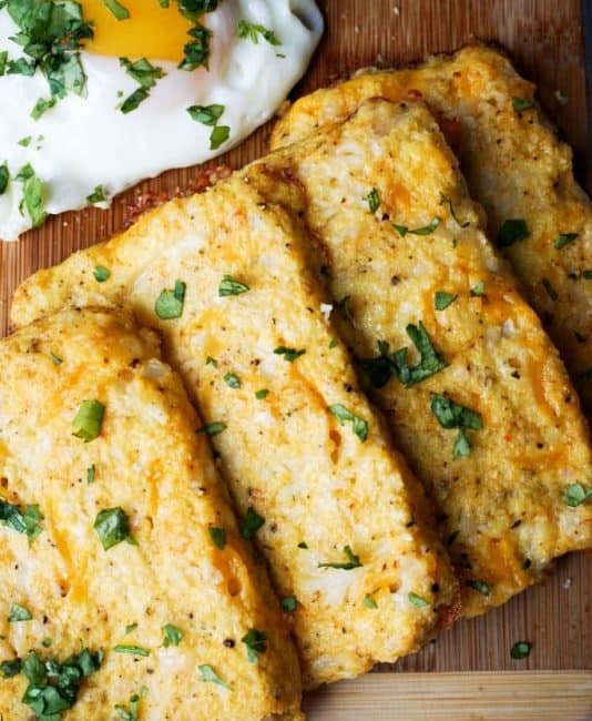 four cauliflower hash browns on a cutting board with an egg