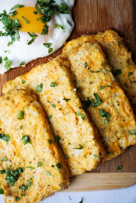 four cauliflower hash browns on a cutting board with an egg