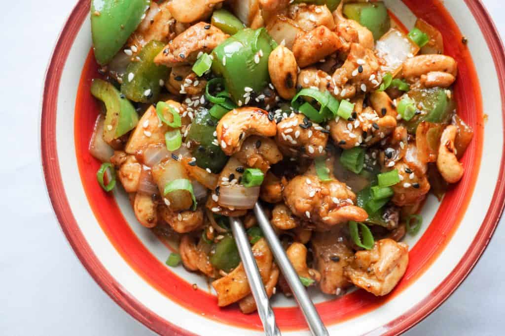 cashew chicken being eaten with chopsticks in a large bowl with a red rim