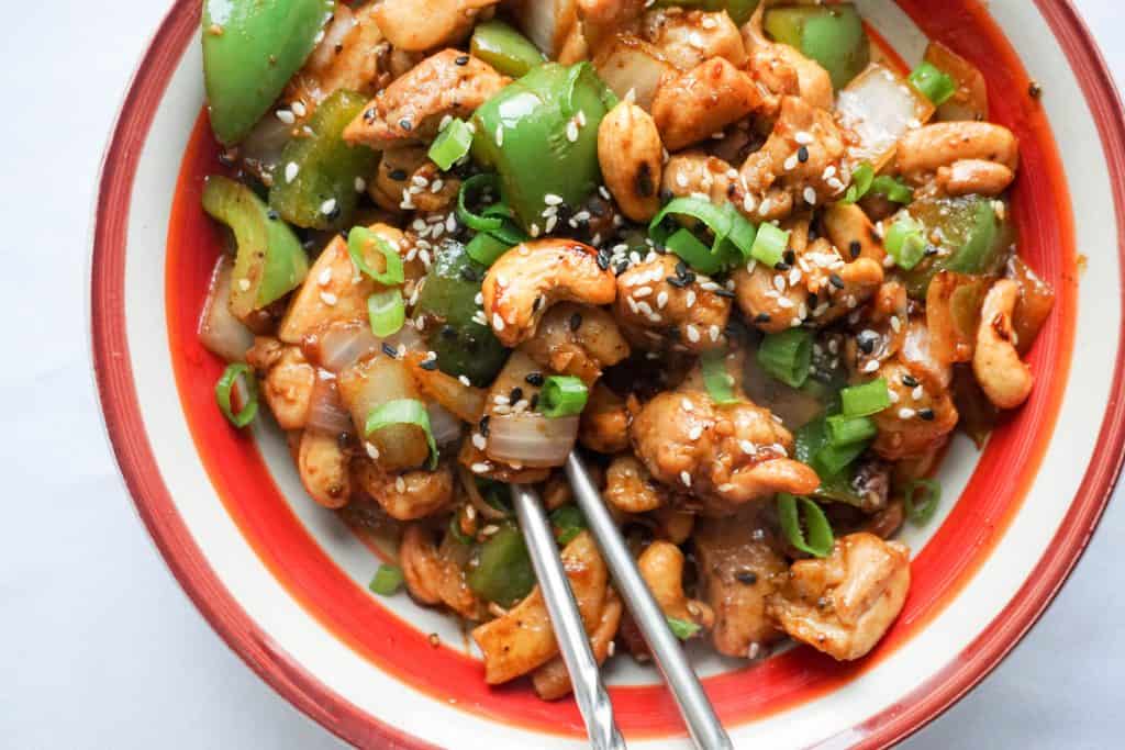 Easy Cashew Chicken cashew chicken being eaten with chopsticks in a large bowl with a red rim