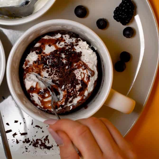 cake in a coffee mug on a plate with spoon taking a piece