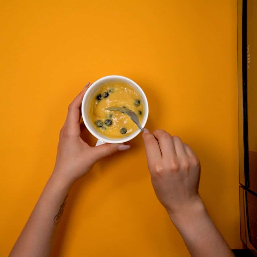 blueberries being mixed into a batter in a coffee mug