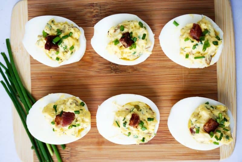 six deviled eggs topped with bacon and diced chives