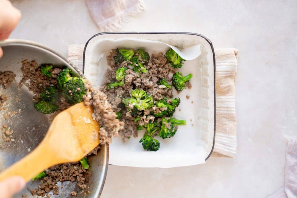 Broccoli and sausage being added to a baking dish