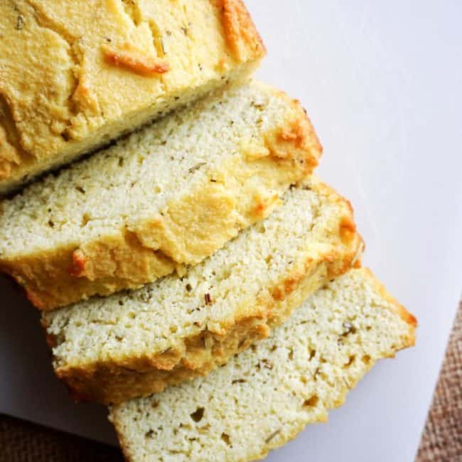 coconut flour bread sliced with rosemary and other herbs on a cutting board