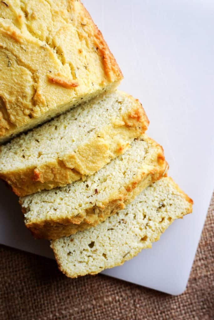 keto coconut flour bread coconut flour bread sliced with rosemary and other herbs on a cutting board