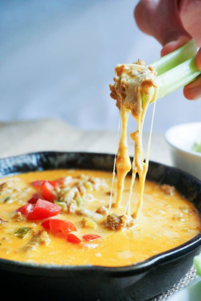 Scooping up keto queso with celery topped with chopped red peppers