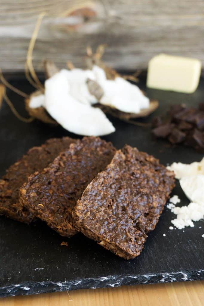 three dark chocolate protein bars in front of a background of coconuts and chocolate