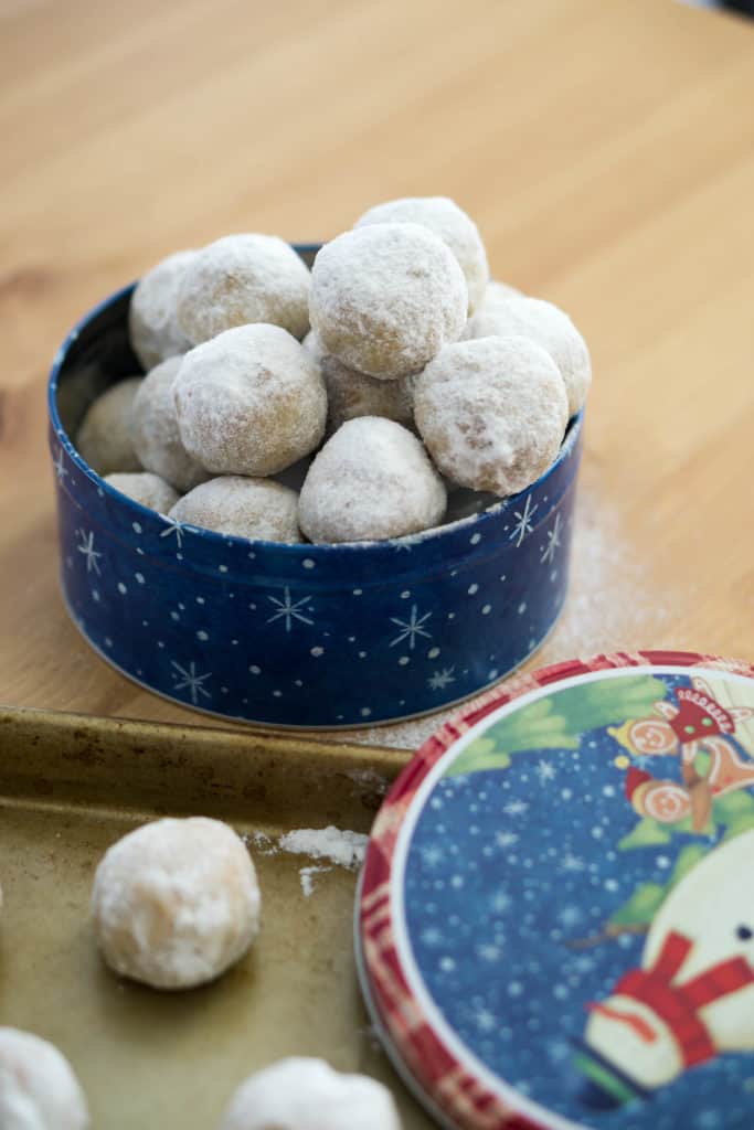 A tin of snowball cookies atop a wood cutting board