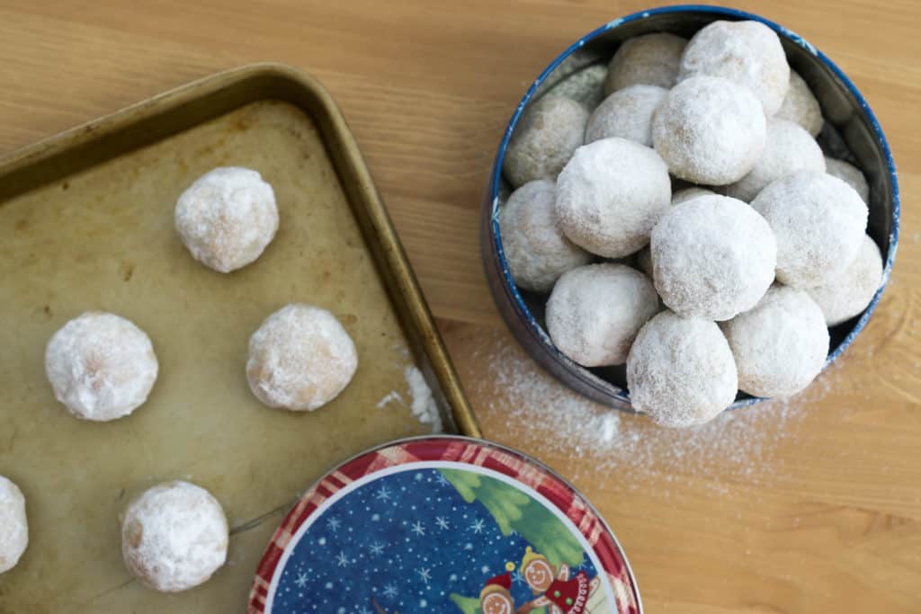 Walnut snowball cookies in a tin next to a baking sheet