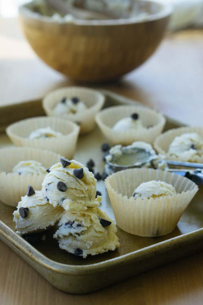 Keto Cookie Dough keto cookie dough fat bombs placed in cupcake liners on a baking sheet with a cookie scoop in the background
