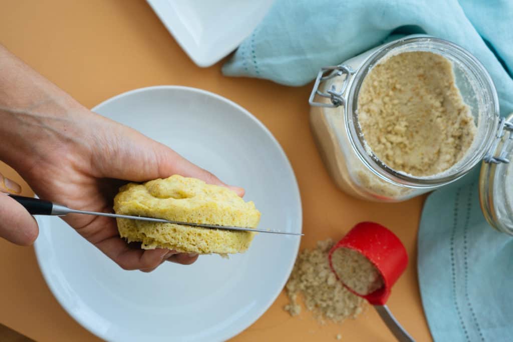 keto mug bread being sliced by hand with a large batch of mix in the background