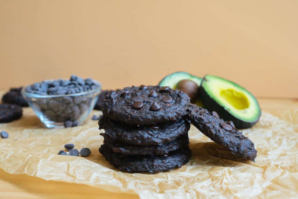 five ultra fudgy avocado cookies next to chocolate chips and avocados