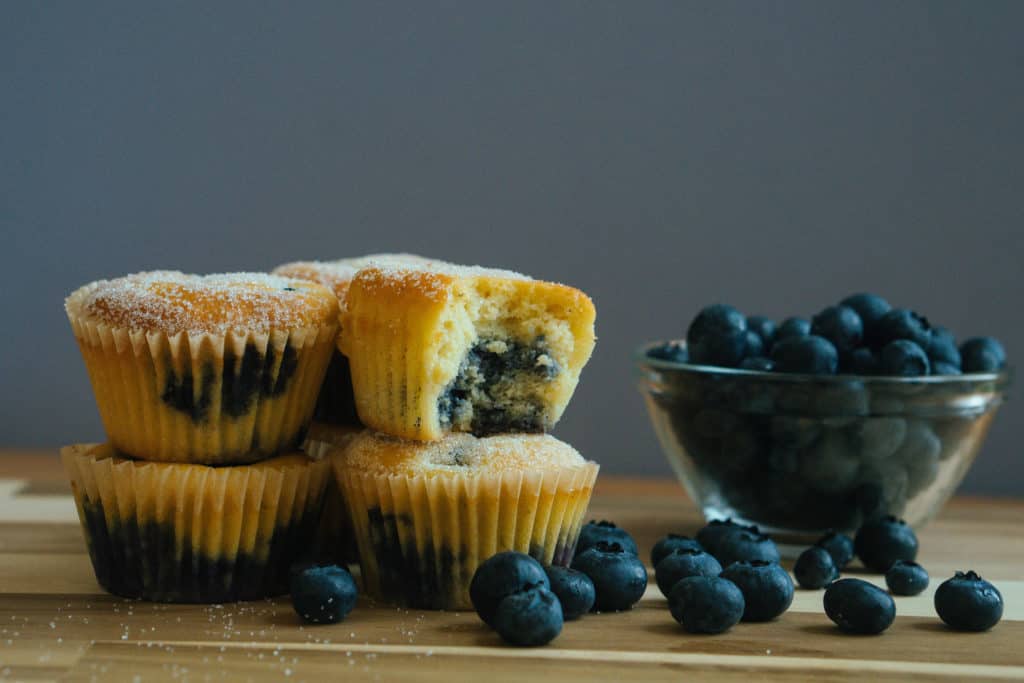 blueberry muffins on a cutting board next to a bowl of blueberries