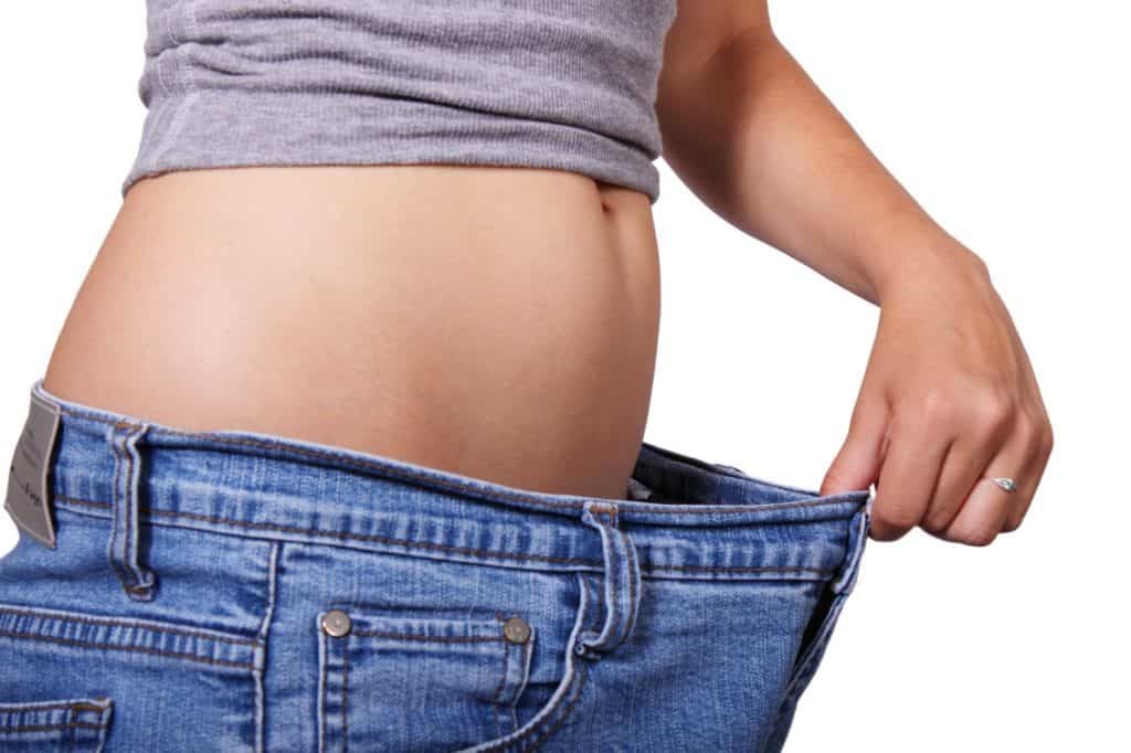 a woman showing how much weight she has lost by stretching the waist of her jeans