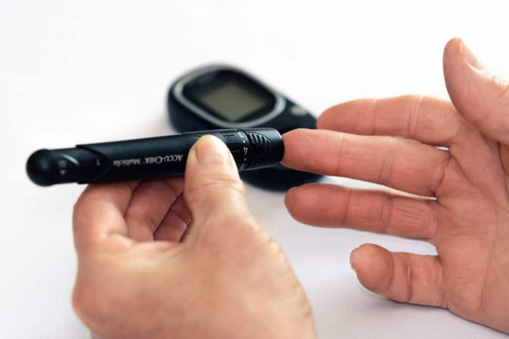 close up image of a man poking his finger with a glucose testing device to test his blood sugar