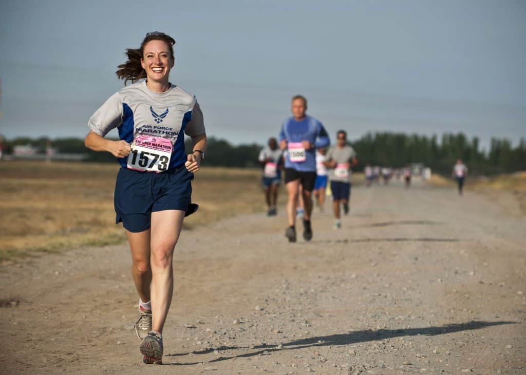 woman with a race bib on running with other runners in the background on a dirt road