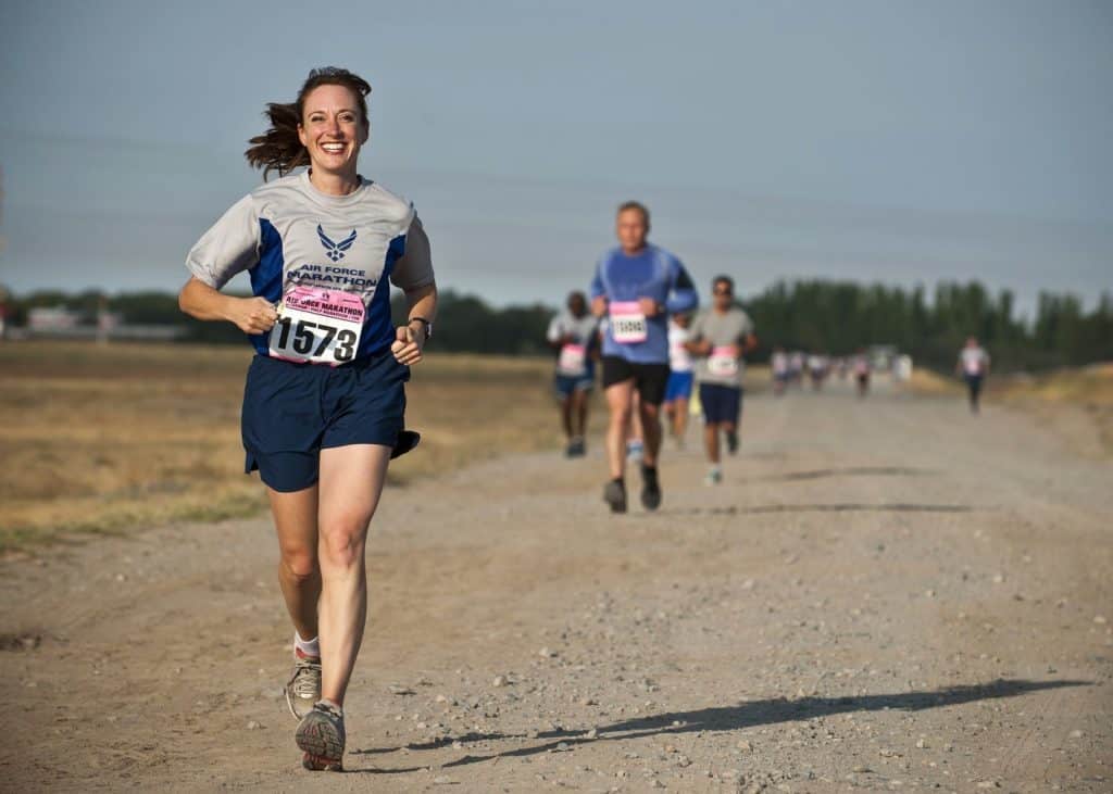ketogenic diet performance woman with a race bib on running with other runners in the background on a dirt road