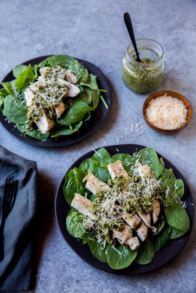 Keto pesto chicken plated next to bowls of pesto and parmesan 