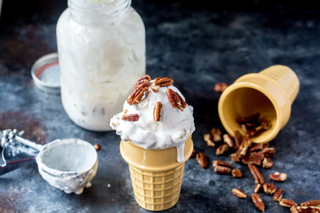 Mason Jar Ice Cream in a ceramic cone topped with pecans next to the ice cream scoop