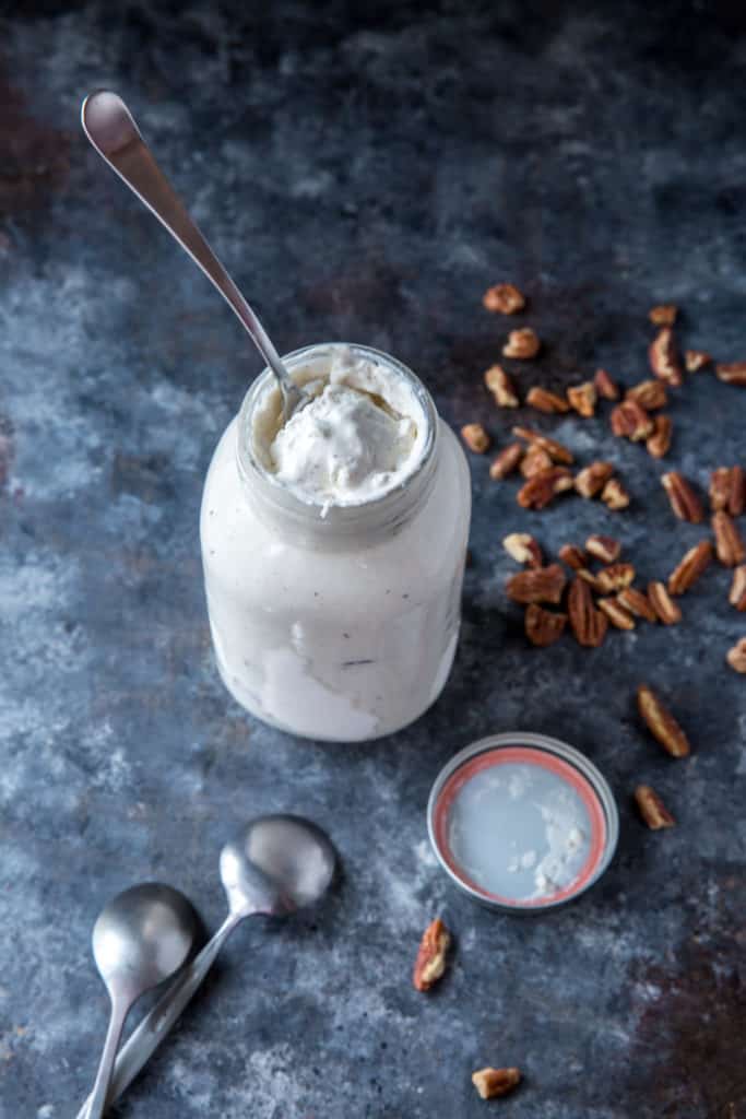 Mason jar ice cream next to two spoons and a handful of chopped pecans