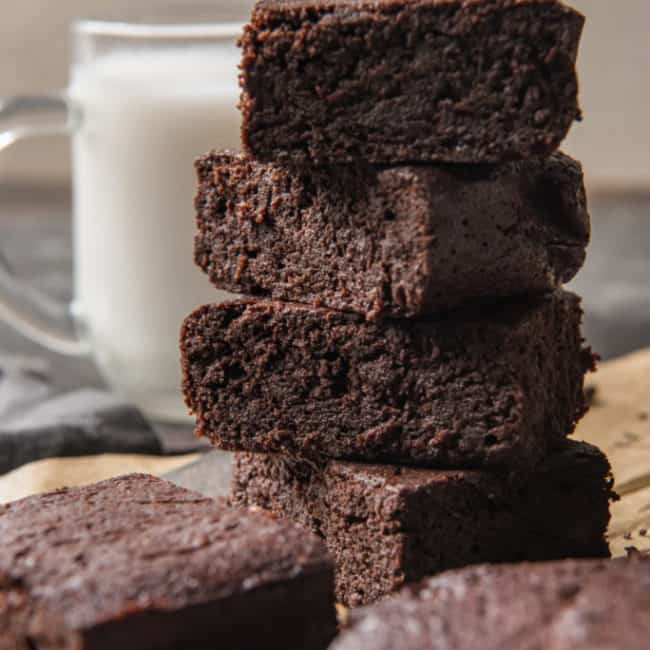 Keto Brownies keto brownies stacked with other brownies in the foreground and a glass of milk nearby