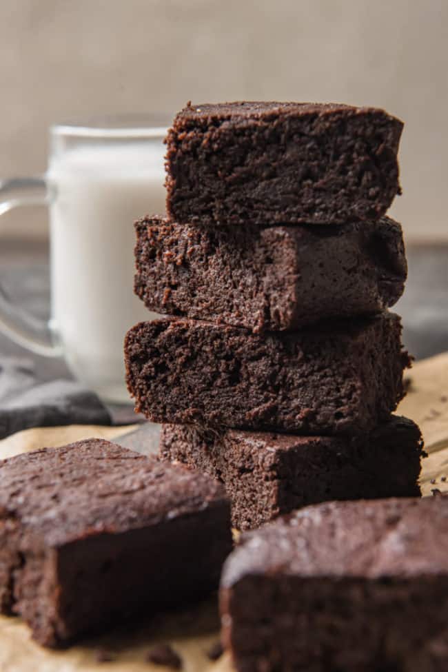 keto brownies stacked with other brownies in the foreground and a glass of milk nearby