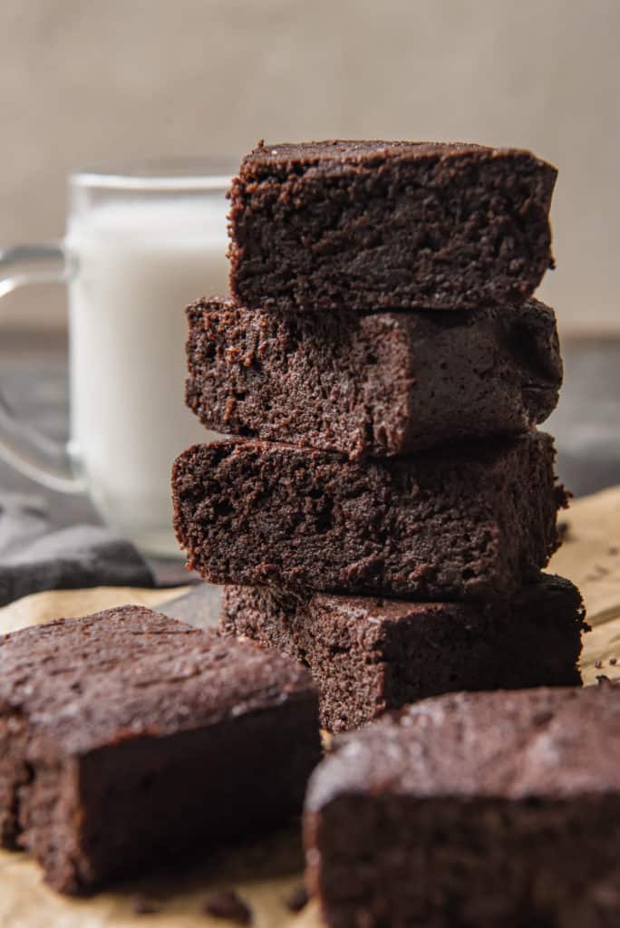 keto brownies stacked with other brownies in the foreground and a glass of milk nearby