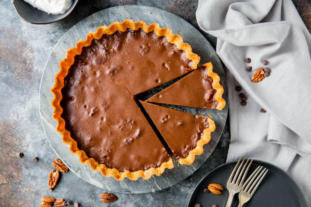 keto dark chocolate pie with two slices cut out on a marble serving platter with a plate and two forks