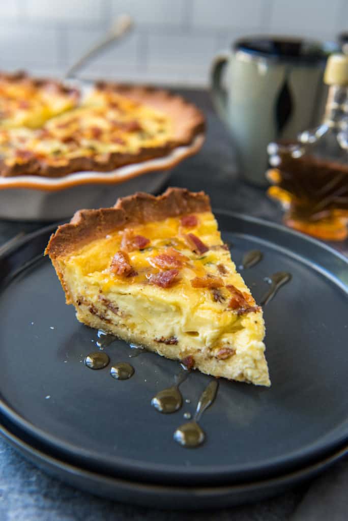 A slice of the bacon and cheese keto quiche served on a black plate drizzled with maple syrup