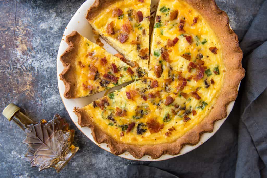 keto quiche horizontal A sliced bacon and cheese keto quiche in a white pie pan with a bottle of maple syrup
