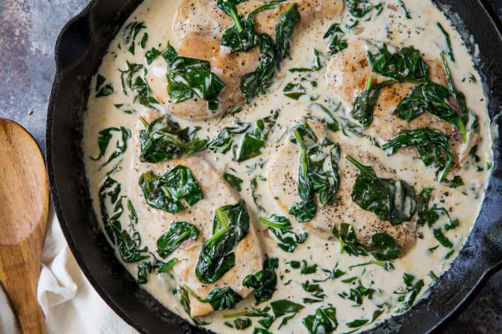 A pan full of chicken floretine with a wooden spoon sitting next to it