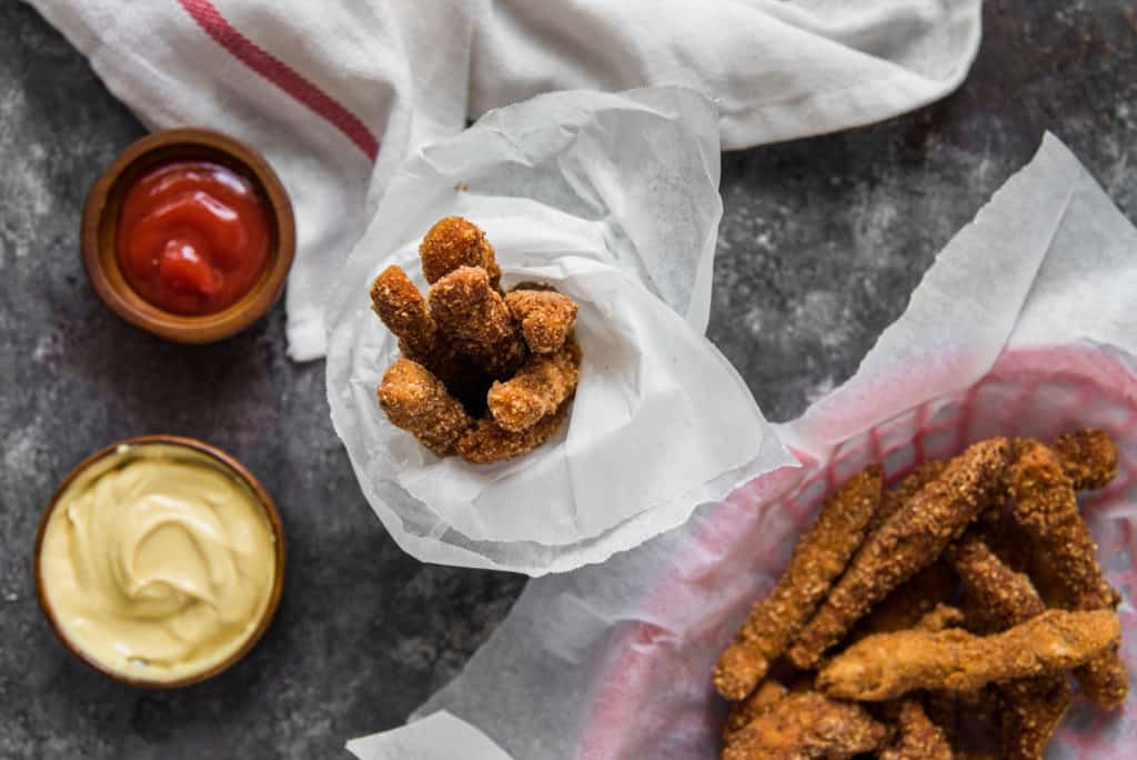 A cup filled with keto chicken fries to the right of ketchup and mayo? 