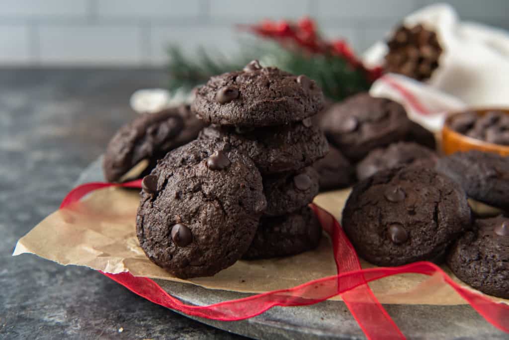 A pile of keto chocolate cookies on brown parchment paper surrounded by red ribbon