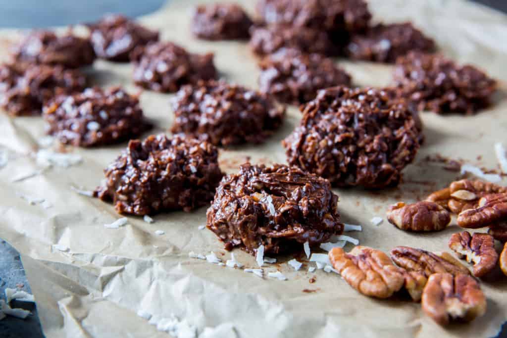 No bake cookies setting on parchment paper beside a handful of pecans. 