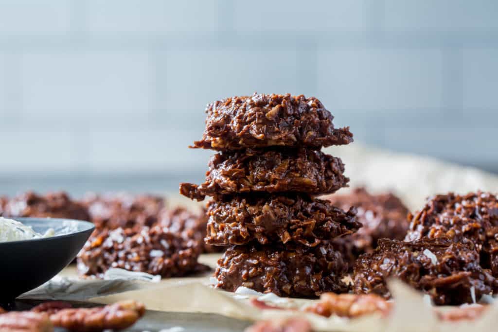 Four keto no bake cookies stacked next to all the other cookies on parchment paper