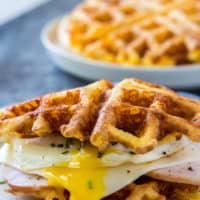 keto chaffles sandwich made with ham and an over easy eagg with a stack of chaffles behind