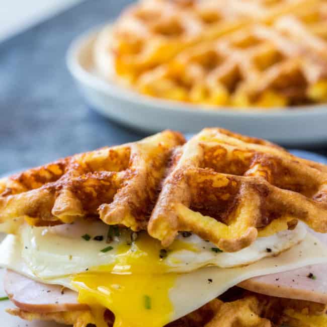 keto chaffles sandwich made with ham and an over easy eagg with a stack of chaffles behind