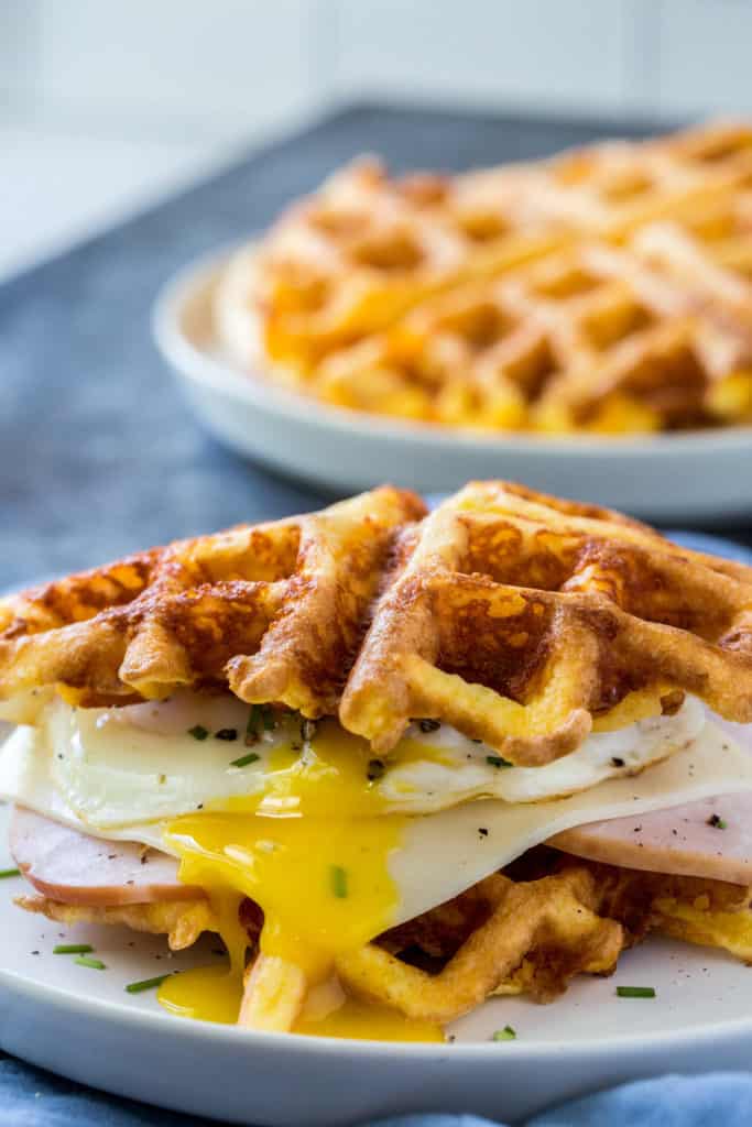 keto chaffles sandwich made with ham and an over easy eagg with a stack of chaffles behind
