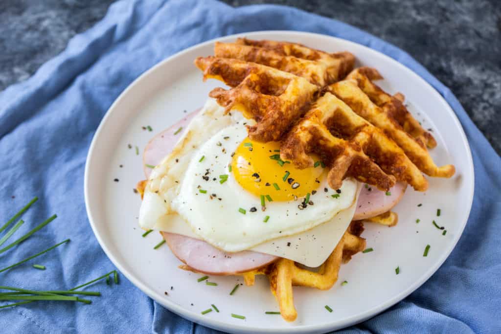 a keto chaffles sandwich using ham and a sunny side up egg on a blue table cloth