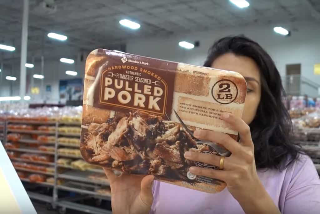 A woman holding a package of fully cooked pulled pork at Sam's Club.
