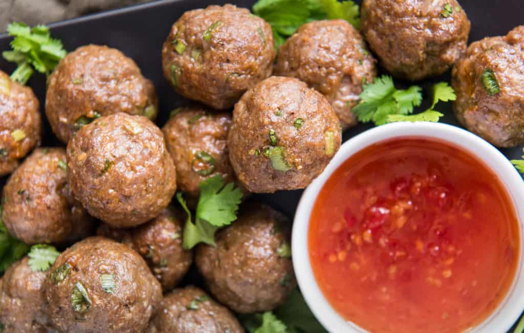 Overhead close up of Meat Balls with a cup of Marinara sauce next to them.