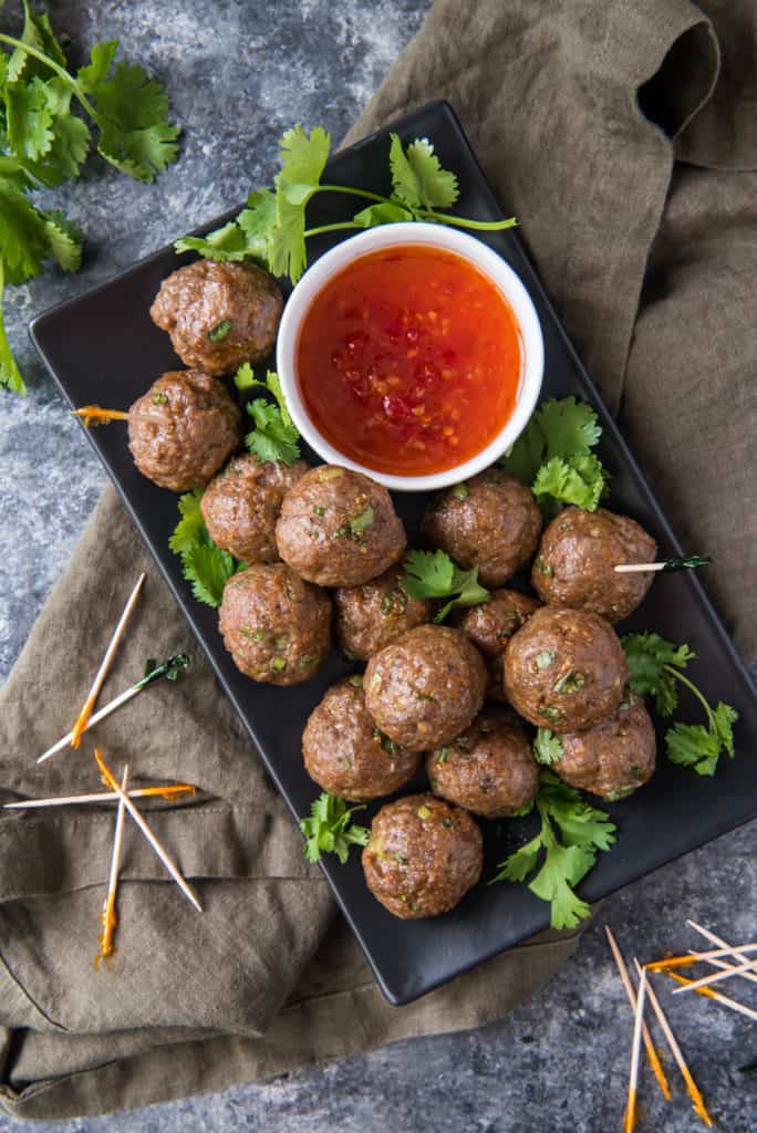 low carb peanut sauce air fryer meatballs on a black tray next to dipping sauce and toothpicks