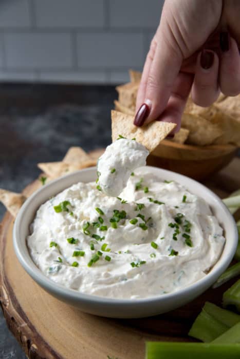 french onion dip in a white bowl with a tortilla chip scooping up some dip