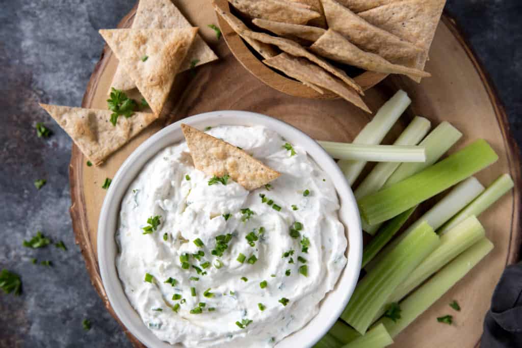 French onion dip served in a white bowl on a wood platter with tortilla chips an celery