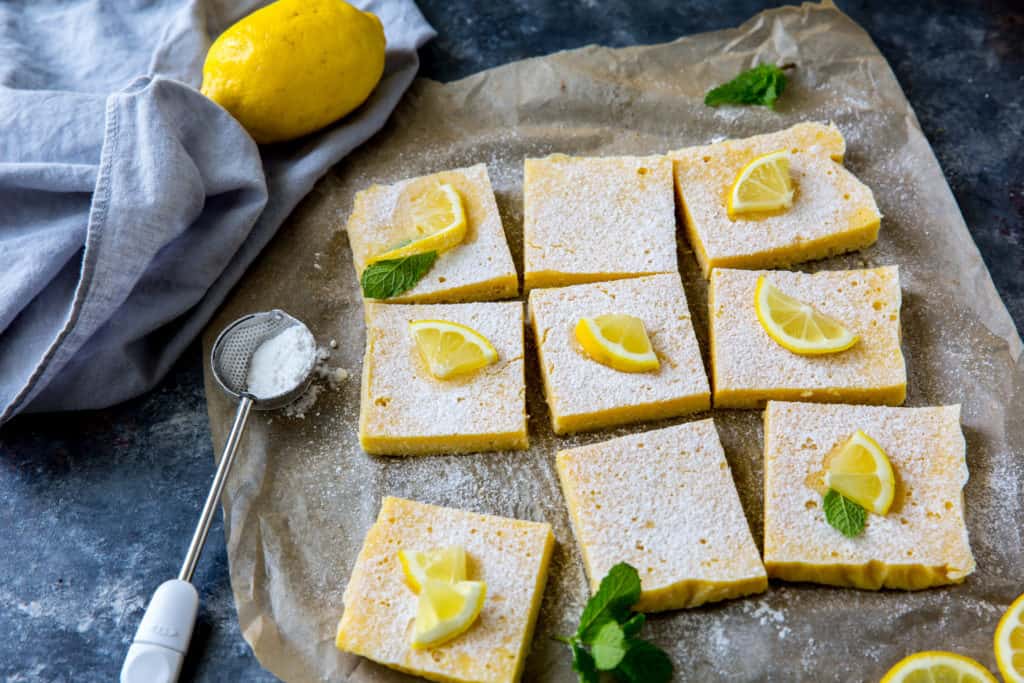 keto lemon bars cut into 9 pieces topped with lemon and mint on parchment paper